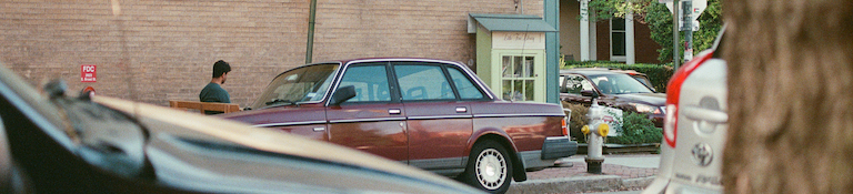volvo 240 parked, view partially blocked by other cars